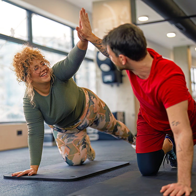 beeld van een lachende vrouw op een matje in de sportschool die een man een high five geeft